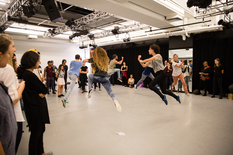 Onlookers watch dancers dart in the air into the center of the room.